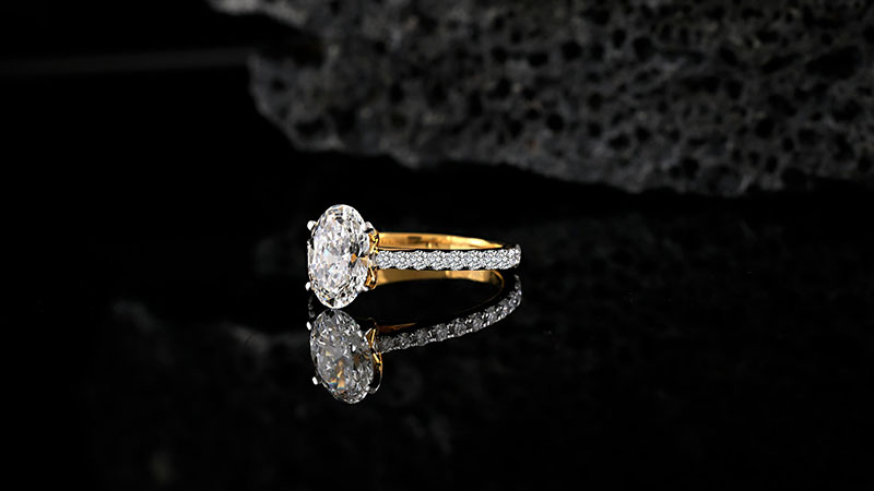 The design surrounds the main stone with small gems, enhancing moissanite’s brilliance.